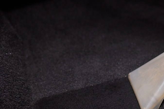 Una mano profesional que utiliza una herramienta de extracción de vacío para limpiar en profundidad una alfombra de coche, mejorando su limpieza.