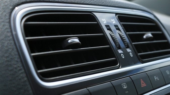 Mano aplicando spray eliminador de olores en las rejillas de ventilación del carro.