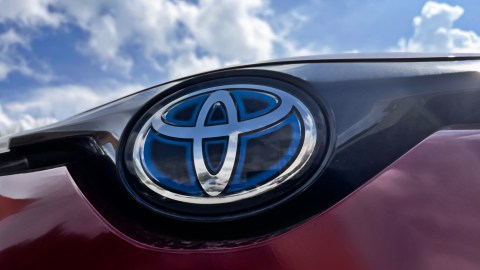 Primer plano del logotipo de Toyota en un automóvil híbrido rojo con reflejo del cielo