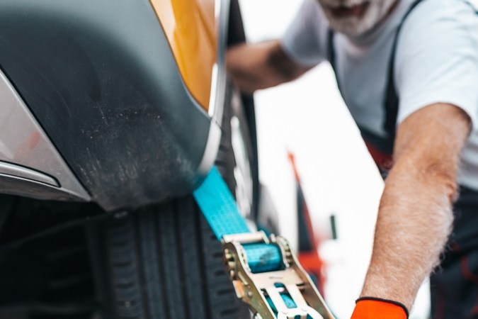 Técnico asegurando carro automático en grúa de cama baja para remolque seguro, evitando daños en transmisión.