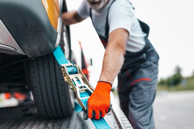 Técnico asegurando carro automático en grúa de cama baja para remolque seguro, evitando daños en transmisión.