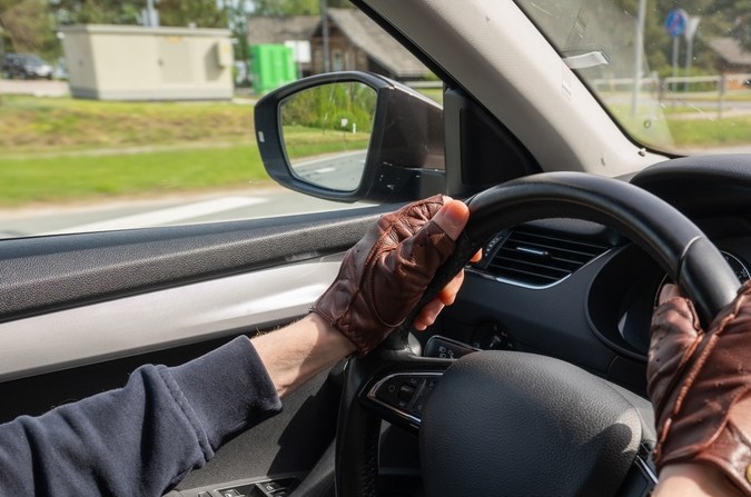 Hombre con guantes de conducción de cuero marrón vintage dirigiendo un coche moderno, tomado desde el interior del vehículo
