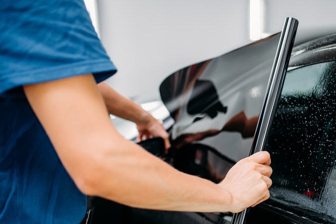 Técnico instalando polarizado en ventana de auto, mostrando técnica y cuidado en taller automotriz.