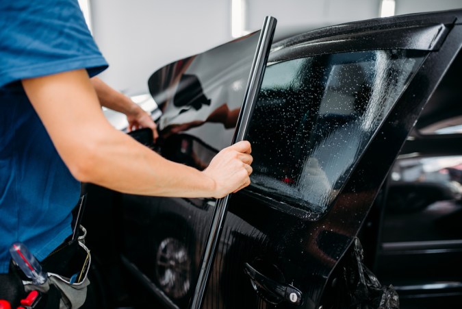 Técnico instalando polarizado en ventana de auto, mostrando técnica y cuidado en taller automotriz.