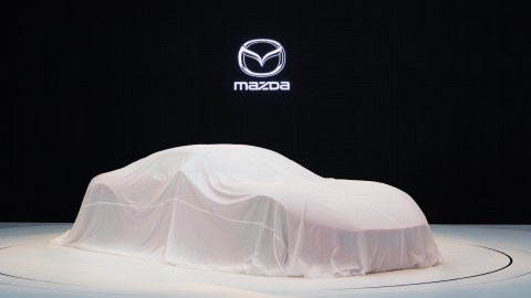 Vwhículo de Mazda cubierto con una lona, anticipando su prsentación en un salón de autos.