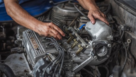 Mecánico ajustando motor con herramientas, mantenimiento automotriz, reparación profesional en taller de coches.