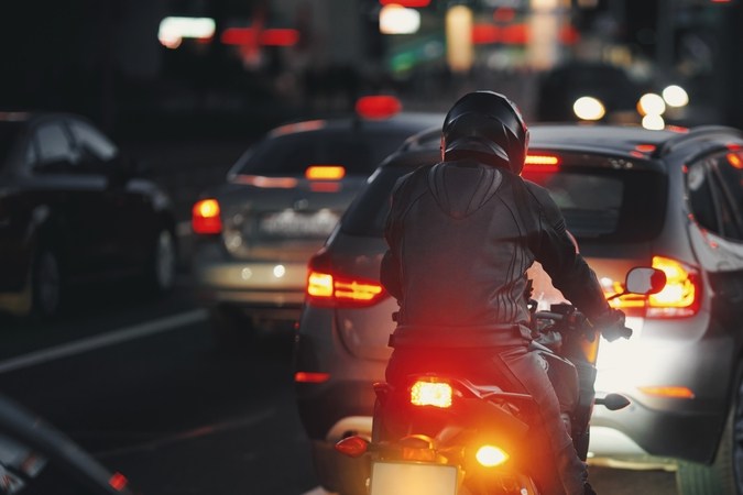 Motociclista en tráfico nocturno ahorrando gasolina con velocidad eficiente entre autos en ciudad.