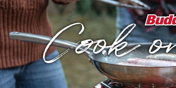 Cocinador portátil BuddyFLEX rojo encendido sobre una mesa de madera, usado para preparar comida al aire libre.