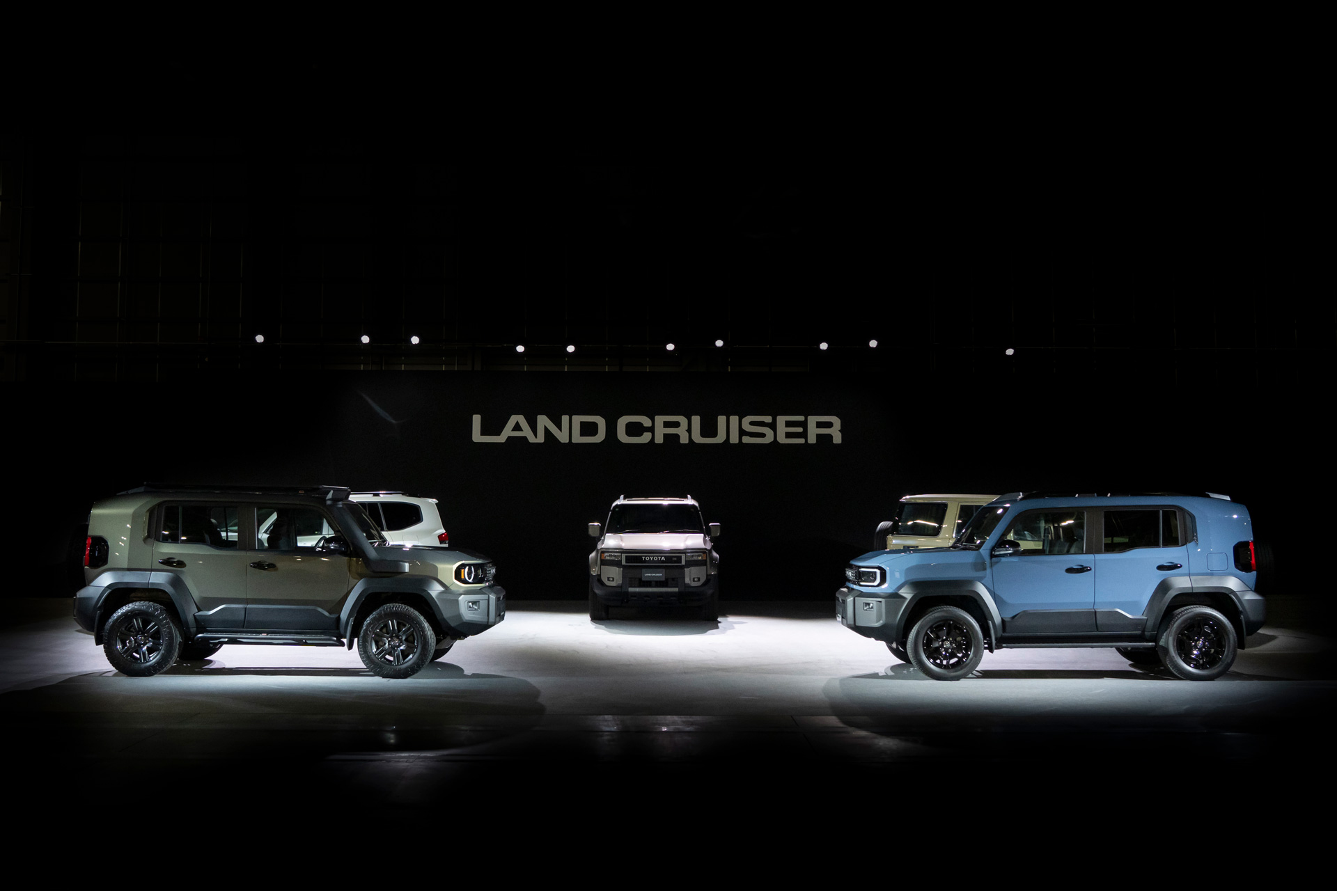 Familia Toyota Land Cruiser FJ 2025: tres SUVs compactos retro bajo logo oficial en exhibición.
