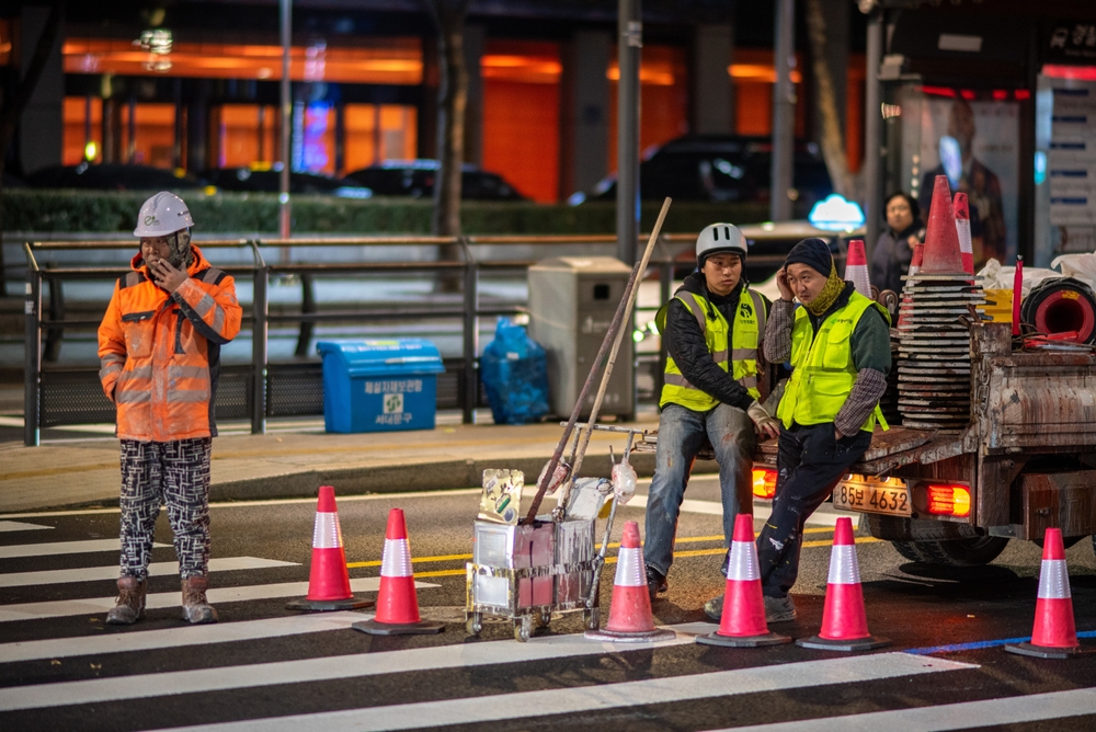 Escena nocturna de trabajo vial con trabajadores y conos de tráfico en Seúl