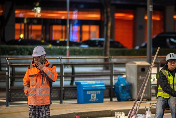 Escena nocturna de trabajo vial con trabajadores y conos de tráfico en Seúl