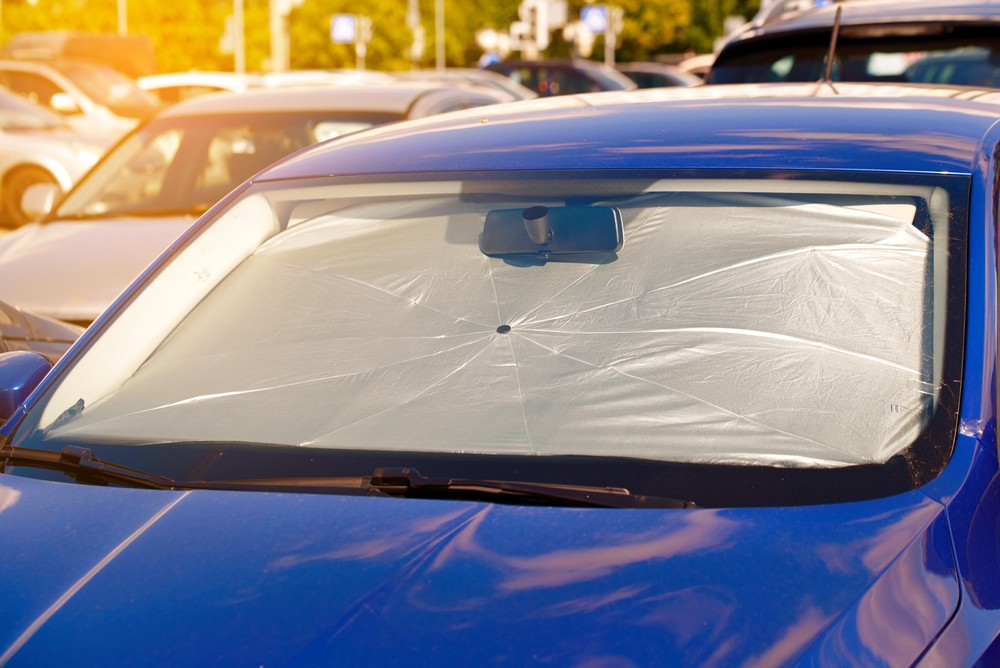 “Automóvil azul estacionado con un parasol blanco cubriendo todo el parabrisas para evitar el calor