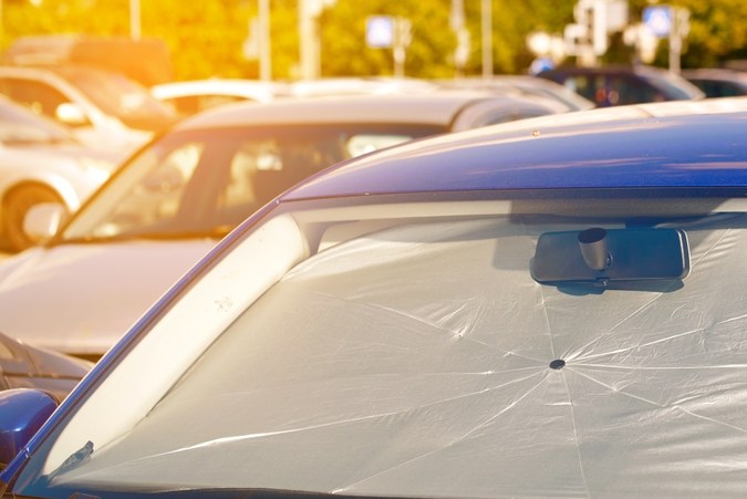 “Automóvil azul estacionado con un parasol blanco cubriendo todo el parabrisas para evitar el calor