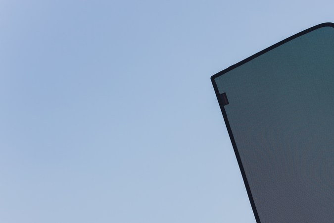 Persona sosteniendo un parasol negro de malla para ventana de carro, con el cielo azul de fondo.