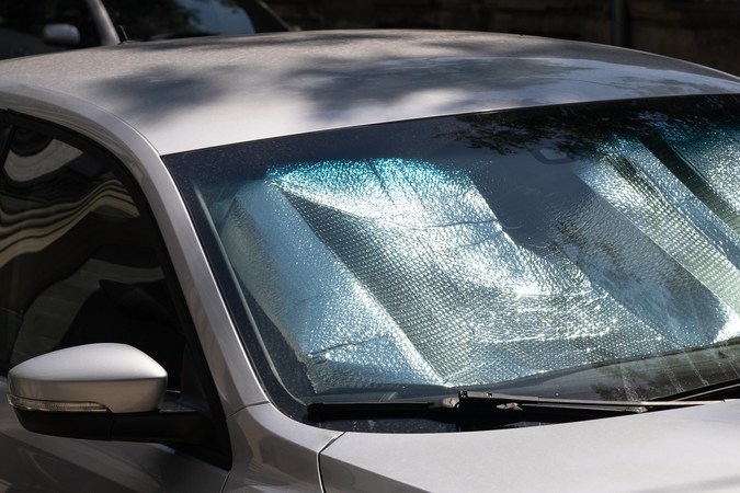 Parasol plateado instalado en el parabrisas delantero de un automóvil plateado estacionado bajo el sol.