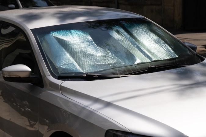 Parasol plateado instalado en el parabrisas delantero de un automóvil plateado estacionado bajo el sol.