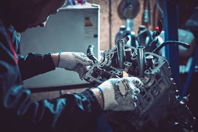 Mecánico trabajando en un motor durante overhaul, reparación de coche en taller, mantenimiento automotriz profesional.
