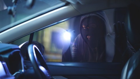 Ladrón afuera de un auto iluminando al interior