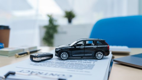 Un escritorio con cartas financieras y documentos de arrendamiento está listo para su revisión. Cerca de allí, una llave del automóvil, un Acuerdo contractual y documentos de seguro esperan las firmas, que representan una transacción de vehículo en curso.