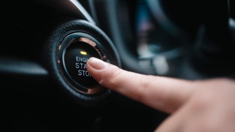 Primer plano de una mano activando el botón Start-Stop en la consola de un vehículo, con fondo oscuro y enfoque en el detalle