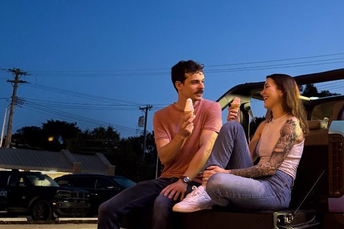 Pareja sentada en la parte trasera de una camioneta eléctrica Slate, disfrutando de un helado durante el atardecer.