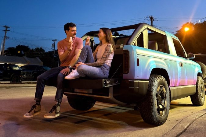 Pareja sentada en la parte trasera de una camioneta eléctrica Slate, disfrutando de un helado durante el atardecer.