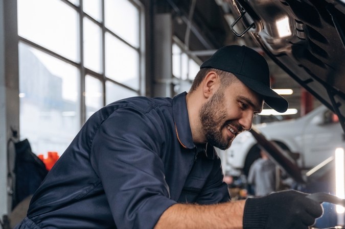 Expresión facial sonriente y alegre. Mecánico trabajando en una estación de servicio de coches.