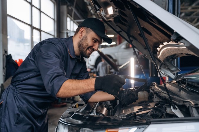 Expresión facial sonriente y alegre. Mecánico trabajando en una estación de servicio de coches.