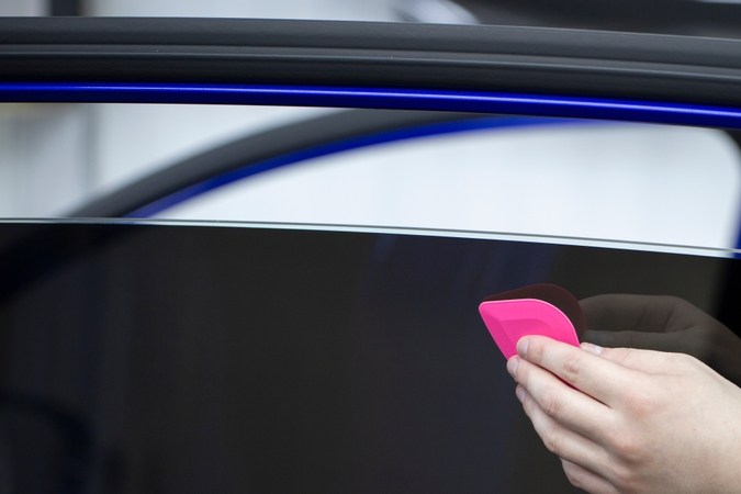 Persona aplicando polarizado oscuro en ventana de auto con herramienta rosa, destacando proceso de tintado profesional.