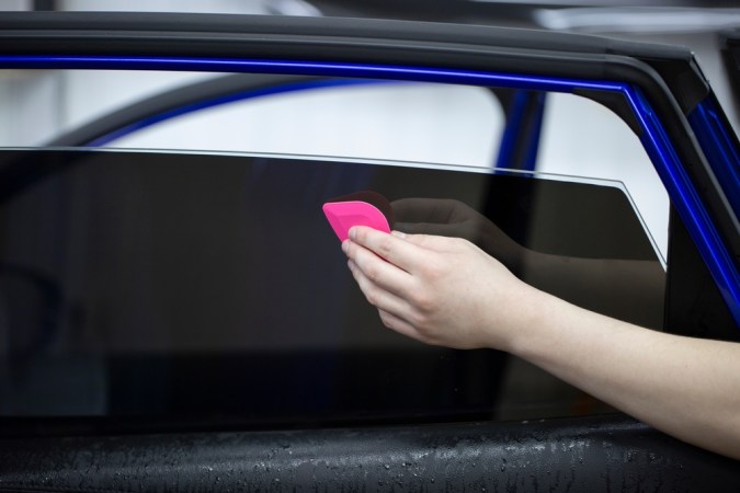 Persona aplicando polarizado oscuro en ventana de auto con herramienta rosa, destacando proceso de tintado profesional.