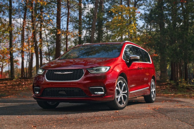 Chrysler Pacifica 2025 roja en bosque otoñal, minivan familiar versátil con diseño moderno y amplio espacio interior para viajes largos.