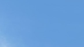 Dos sedanes Toyota Camry 2026, uno gris y otro azul, estacionados en una plaza adoquinada con árboles, quiosco y banderines bajo cielo despejado.