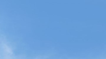 Dos sedanes Toyota Camry 2026, uno gris y otro azul, estacionados en una plaza adoquinada con árboles, quiosco y banderines bajo cielo despejado.