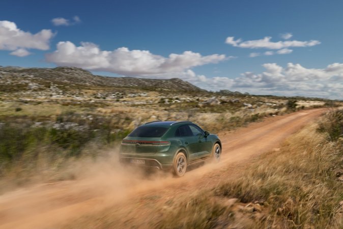 Porsche Macan 4S verde 100% eléctrico, rodando rápido en pista de tierra panorámica, SUV premium deportivo de lujo y alto rendimiento.