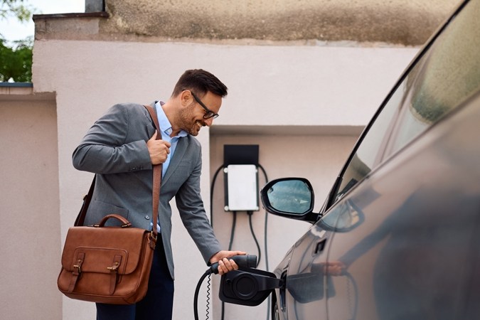 Hombre feliz enchufando su coche eléctrico al Recargo.