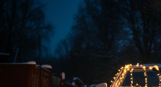 Vista frontal del coche moderno decorado con luces de Navidad Noche de país nevado