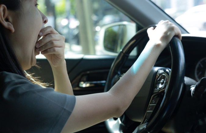 Mujer somnolienta mientras conducía por la carretera. Concepto de salud y seguridad en la conducción. Mujer con sueño bostezando. Una mujer conduce un auto con mal atasco en hora punta. somnoliento mientras conduce. accidente de carretera