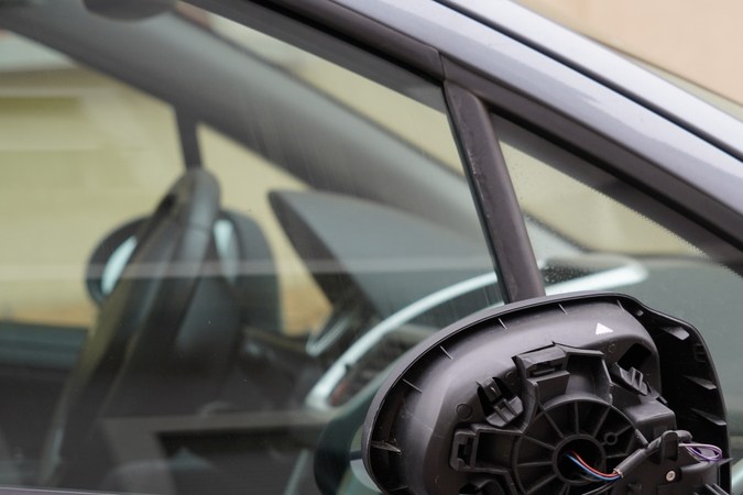 Cierre la vista sobre el espejo retrovisor de la puerta ajustable roto o el espejo de ala fabricado con plástico negro. De la tapa desmontada, que se pega a los cables eléctricos rojos y azules. En parte se ve un interior desenfocado.