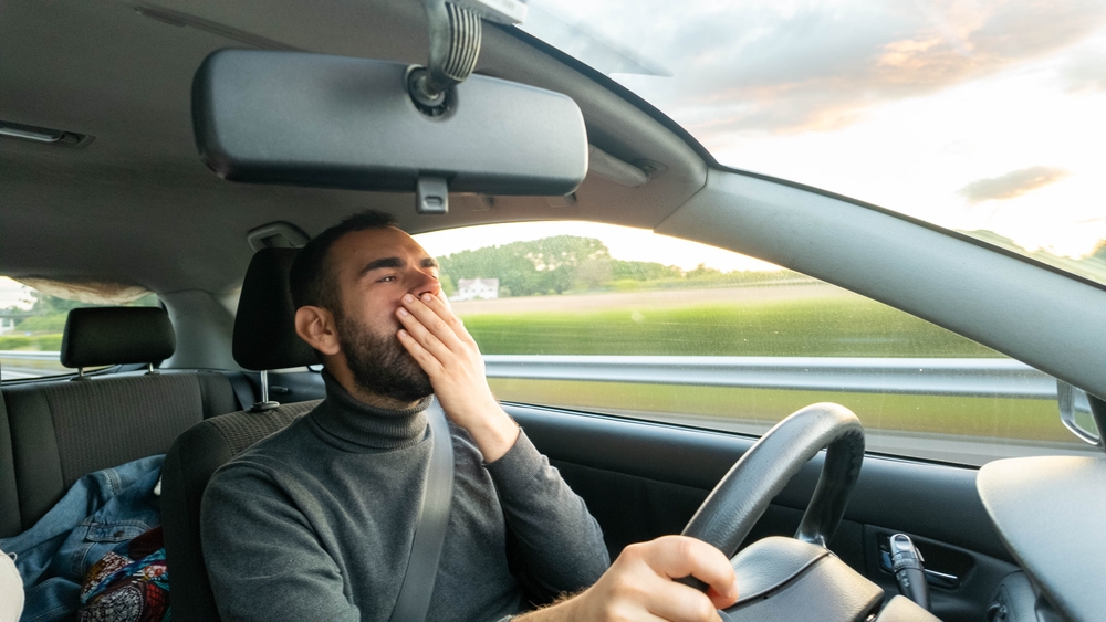 Joven cansado bostezando mientras conduce durante la puesta del sol.