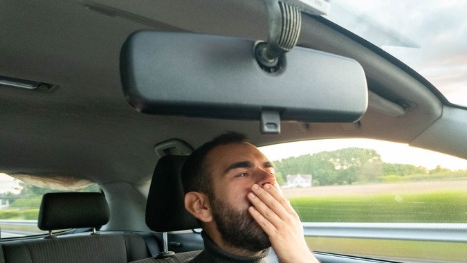 Joven cansado bostezando mientras conduce durante la puesta del sol.