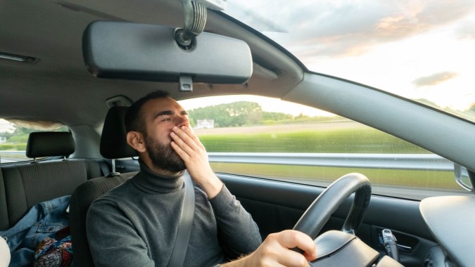 Joven cansado bostezando mientras conduce durante la puesta del sol.