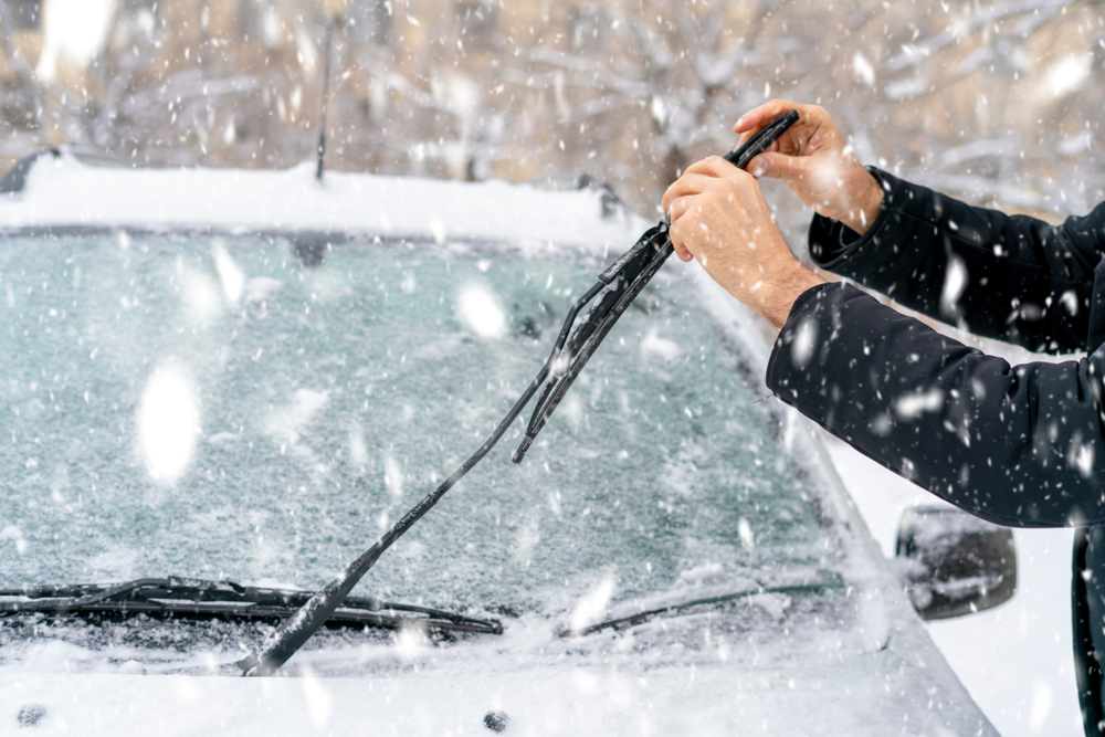 hombre ajustando y limpiando limpiaparabrisas de camión en tiempo nevado