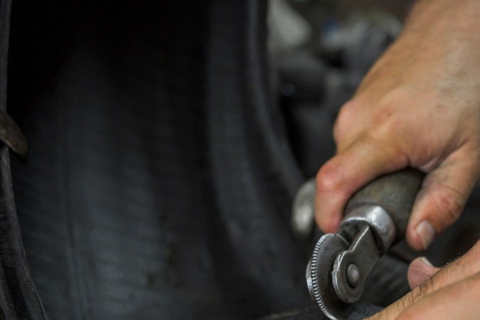 cierre las manos de un hombre que talla un neumático con una herramienta de mano para vulcanizar el neumático y parchearlo