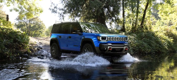 Jeep Recon 2026 azul cruzando agua, demostrando resistencia y tecnología 4x4 eléctrica en entorno natural forestal.
