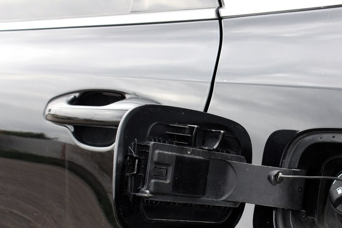 Primer plano de un área de llenado de combustible de automóvil negro con tapa de gas abierta. La gorra negra mate contrasta con el cuerpo pintado brillante. La escotilla del tanque diesel, la escotilla del tanque de gasolina, la escotilla del tanque de combustible está abierta en el coche.