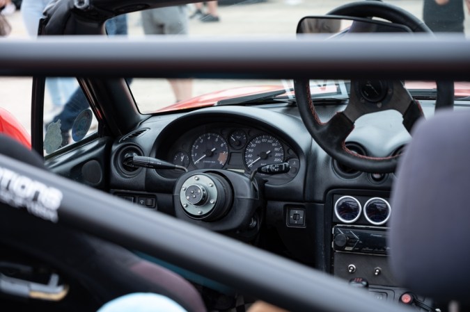 Un primer plano de la cabina interior de un clásico Mazda Miata NB. El deportivo JDM se ha modificado con un volante de Autorización rápida y una barra antivuelco con especificaciones de carrera