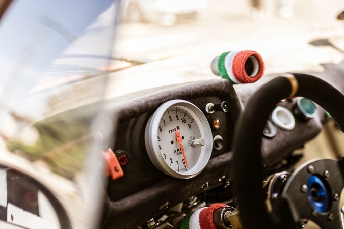 primer plano de un tablero de instrumentos de un automóvil de carreras con un contador de revoluciones, volante y detalles de la bandera italiana, que evocan velocidad y competencia