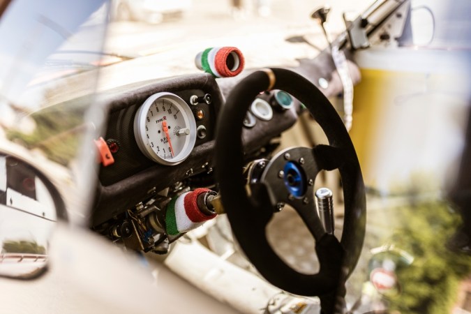 primer plano de un tablero de instrumentos de un automóvil de carreras con un contador de revoluciones, volante y detalles de la bandera italiana, que evocan velocidad y competencia