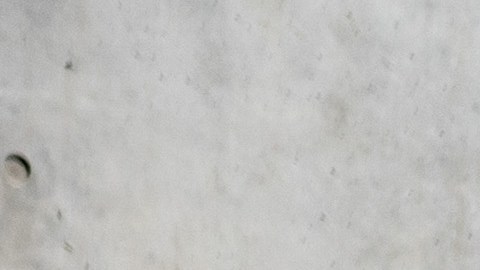 Vista tres cuartos del Nissan Versa 2025 rojo frente a arquitectura moderna, exhibiendo el diseño exterior renovado de este auto económico descontinuado.