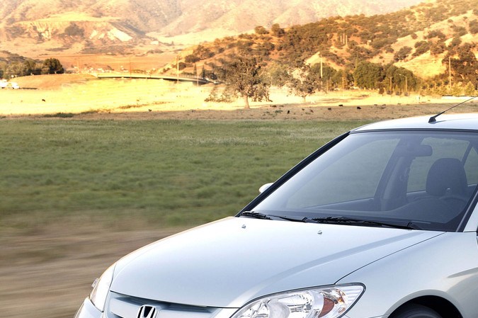 Honda Civic Hybrid 2004 plata circulando por carretera rural, sedán híbrido usado eficiente en combustible.